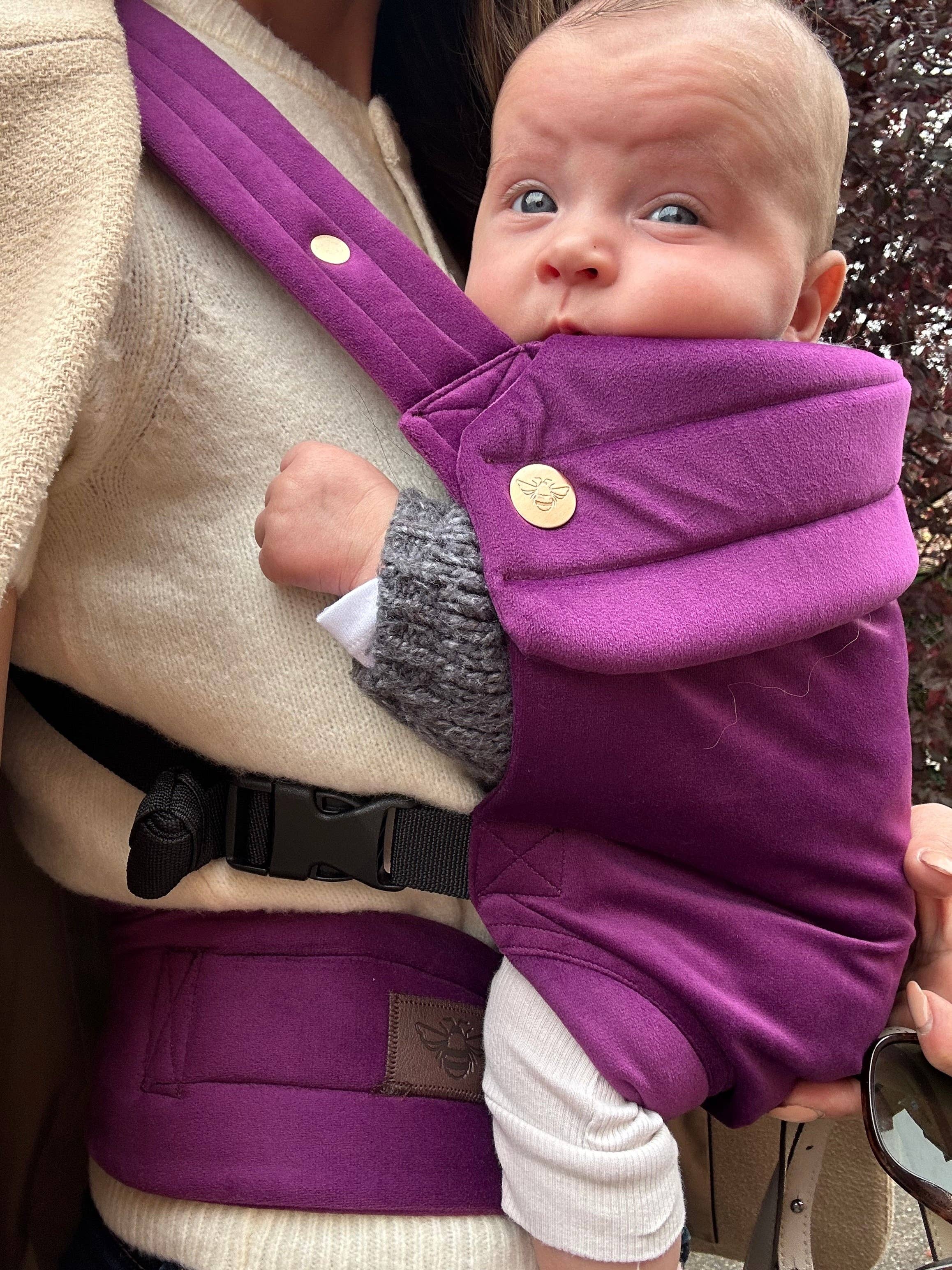 Baby in a purple carrier held by a person outdoors
