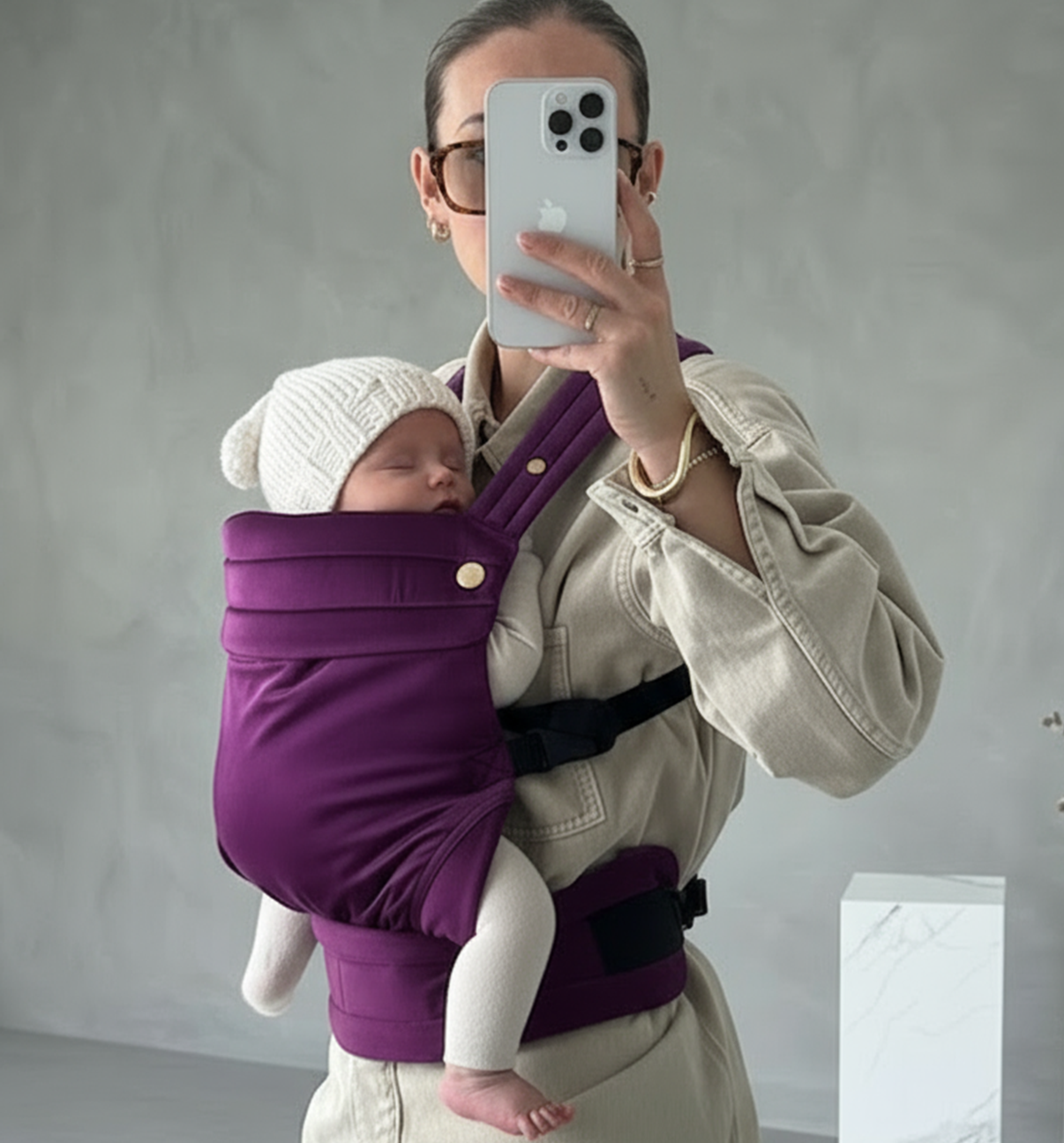 Person holding a baby in a purple carrier against a plain background