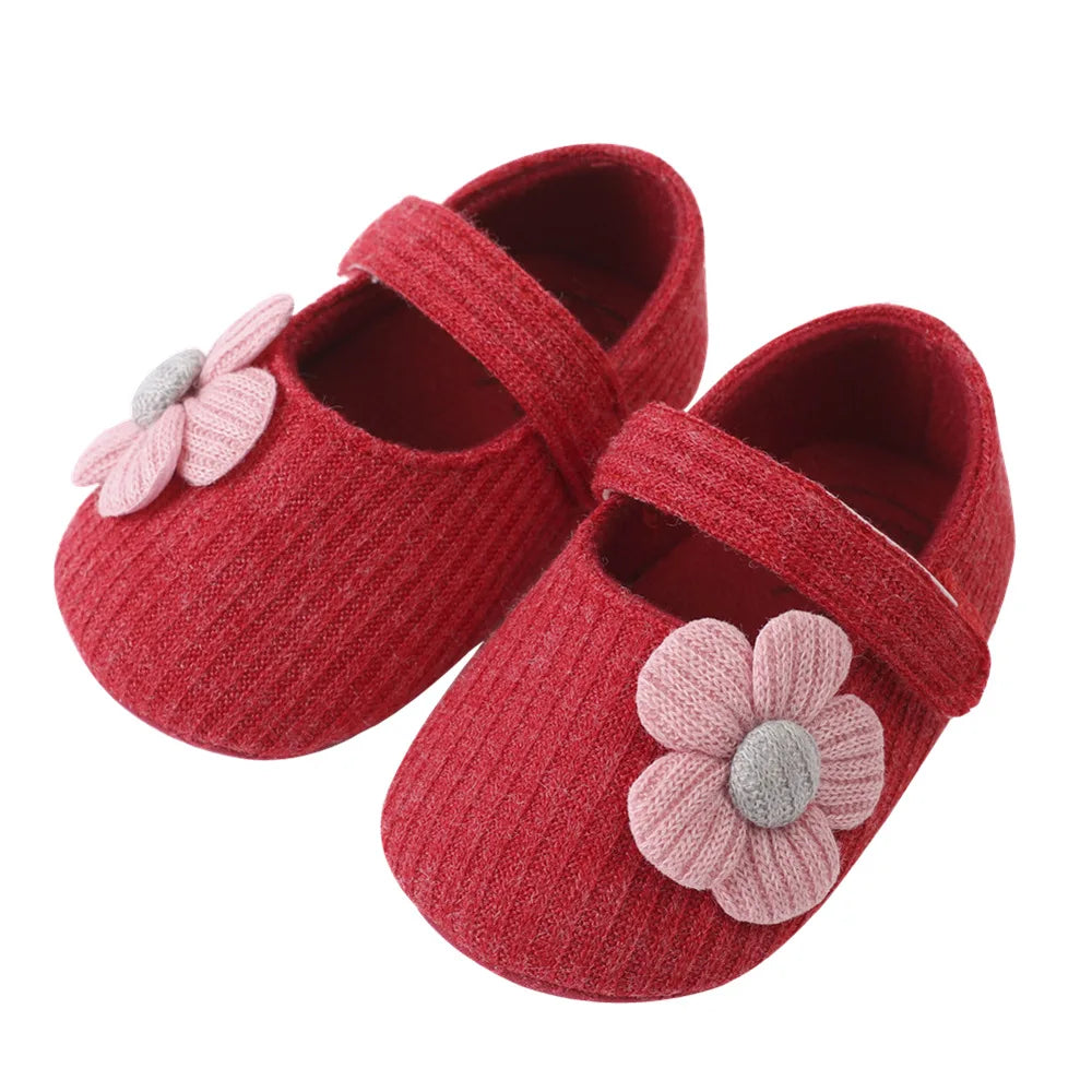 Red baby shoes with pink flower decorations on a white background