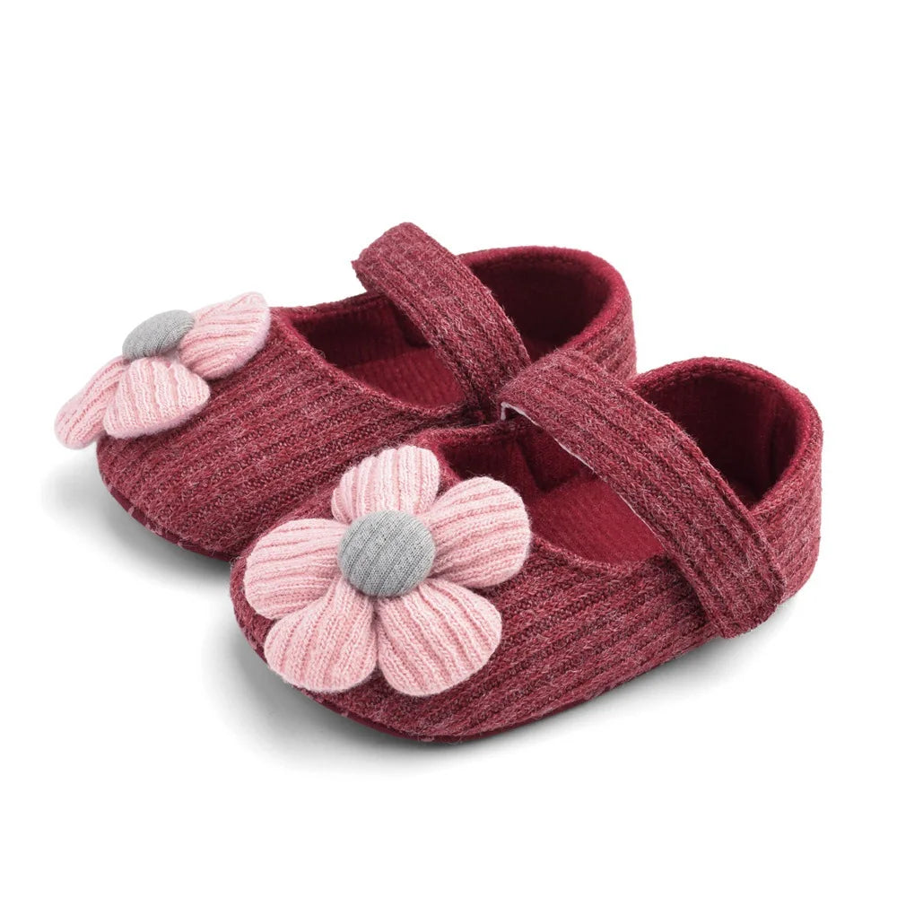 Red baby shoes with pink flower decorations on a white background