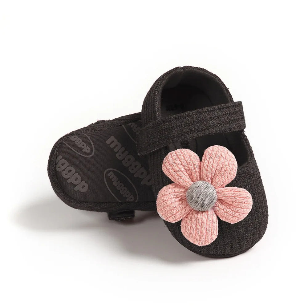 Black baby shoe with a pink flower on a white background