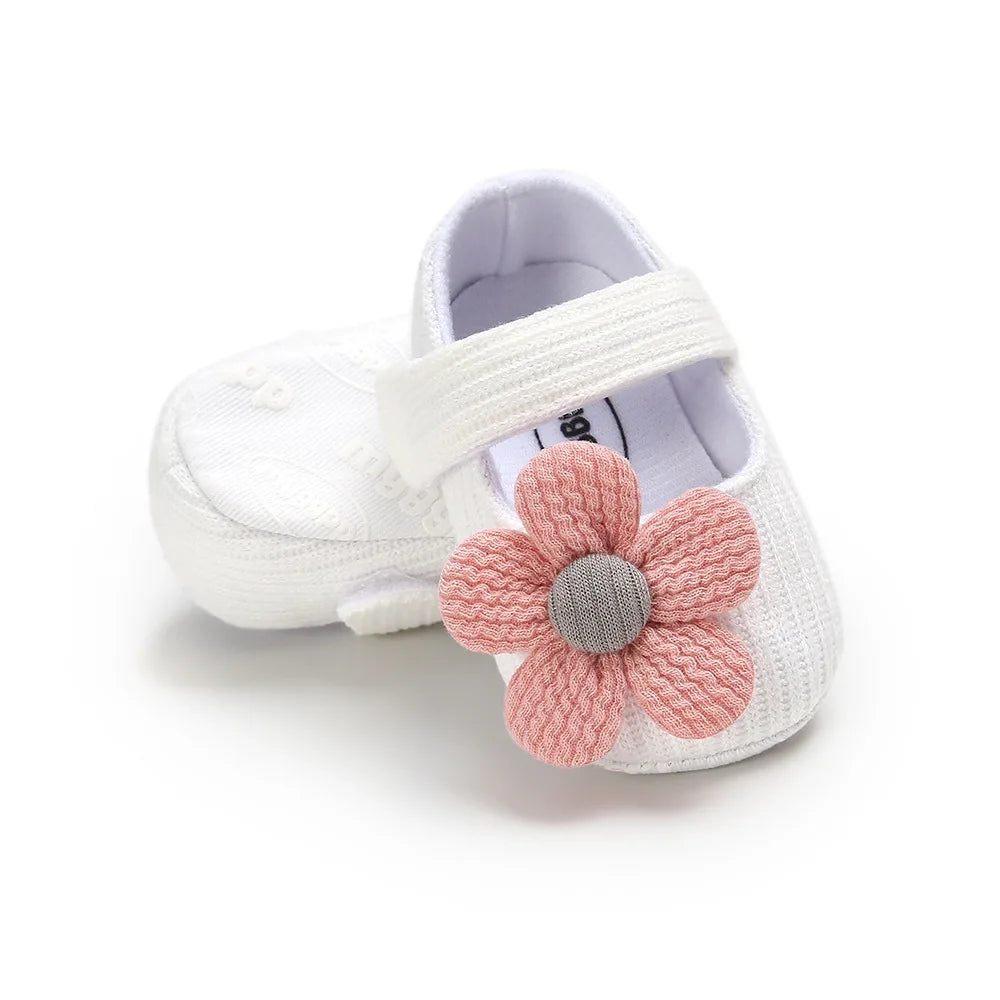 White baby shoe with a pink knitted flower on a white background